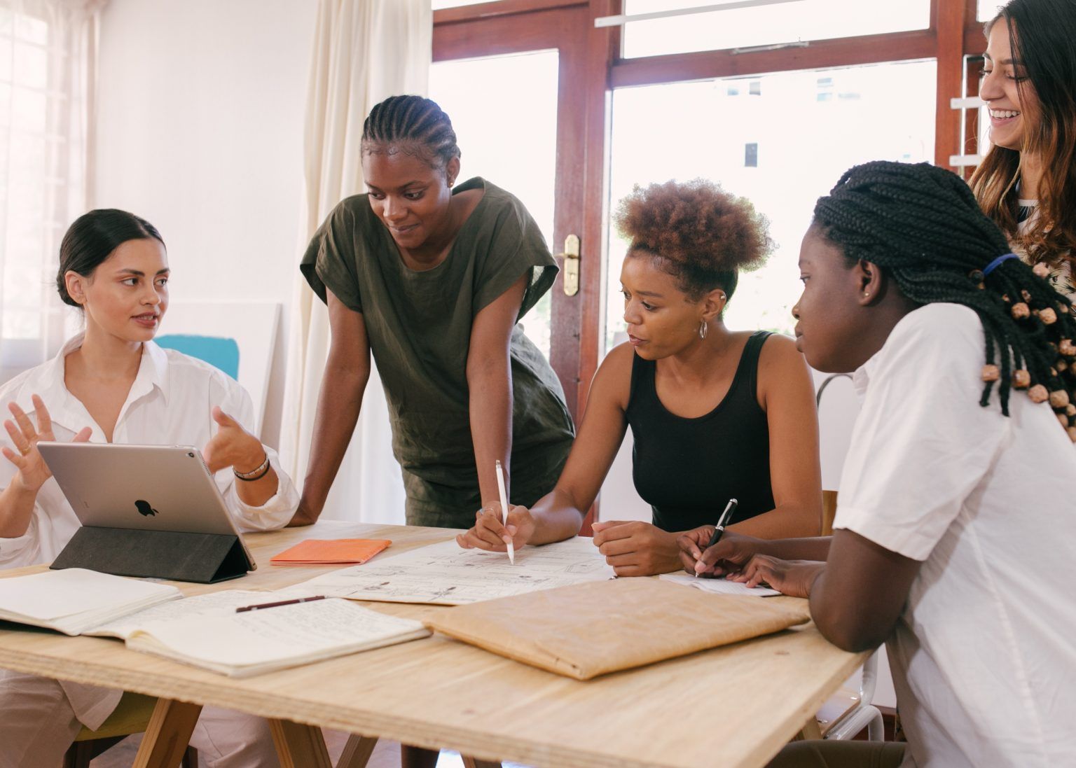 Five people gathered around a table, annotating a hand-drawn plan together during a working session.